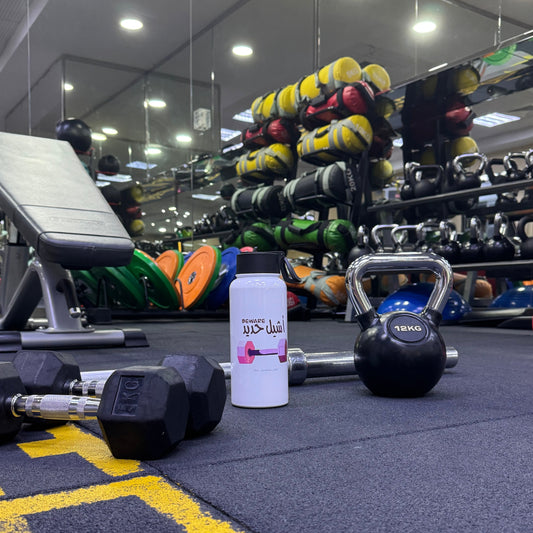 Gym equipment including dumbbells, kettlebell, and a white container with Arabic text on a blue floor.