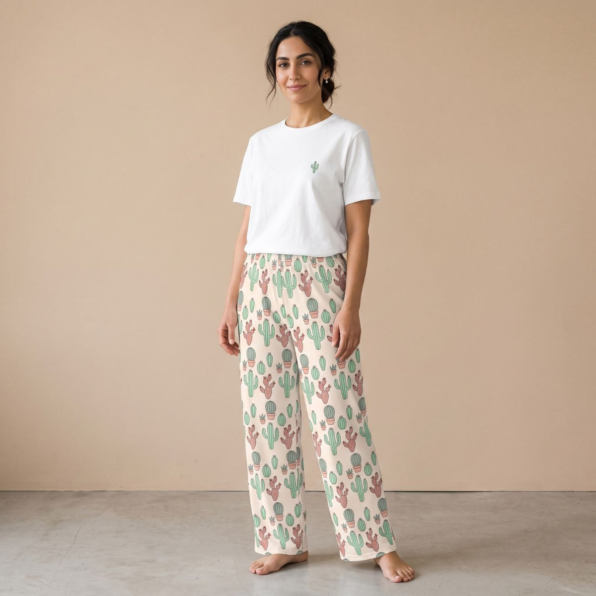 Model wearing a white T-shirt with a small cactus motif and cream pants with green and pink cactus prints, front view.