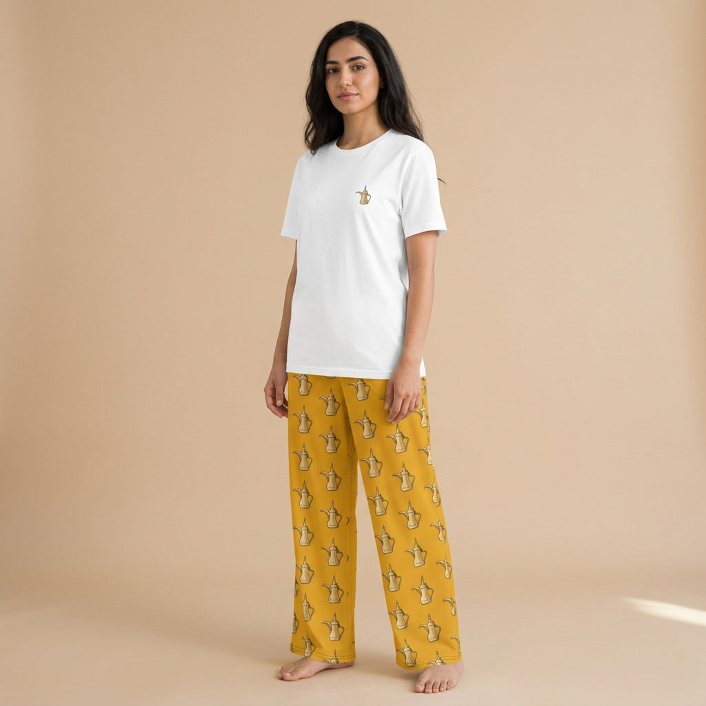 Model wearing a white T-shirt with a small Arabic coffee pot motif and mustard-yellow wide-leg pants with a matching all-over pattern.