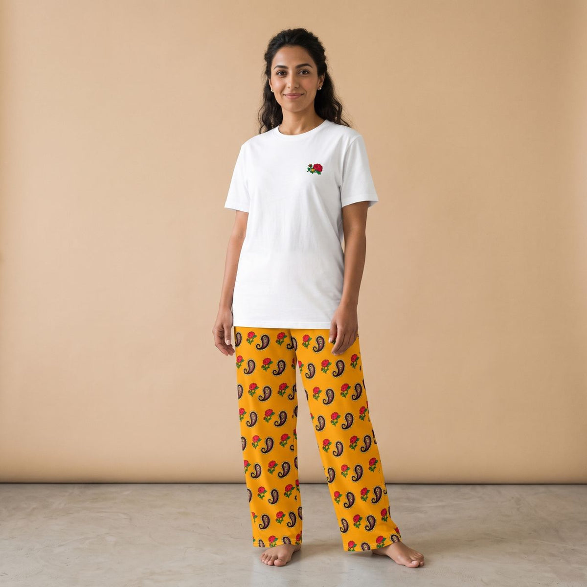 Model wearing a white T-shirt with a small red rose motif and golden yellow pants with rose and paisley prints, front view.