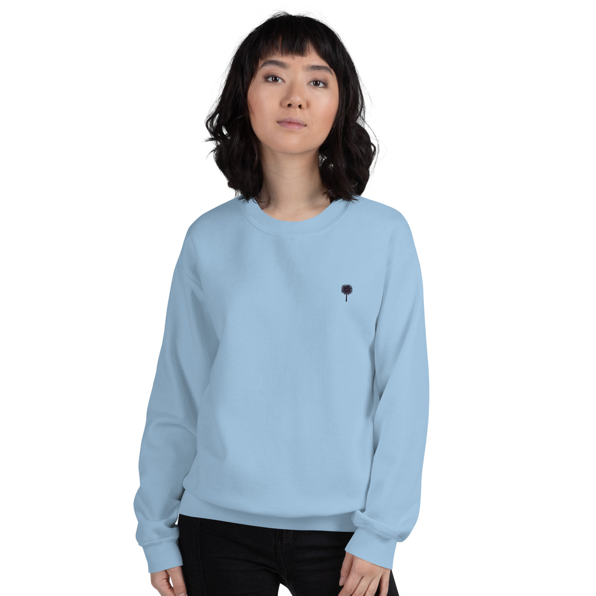 Person wearing a light blue sweatshirt with a small black palm tree embroidered design on a white background