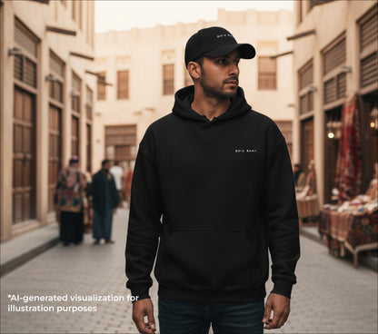 Man wearing a black hoodie and cap with the text "80's baby" embroidered on them in an outdoor setting with people and buildings in the background.