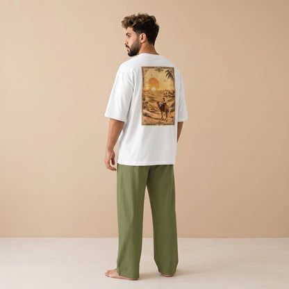 Man wearing a white oversized T-shirt with a desert sunset and camel rider graphic on the back, paired with olive green wide-leg pants.