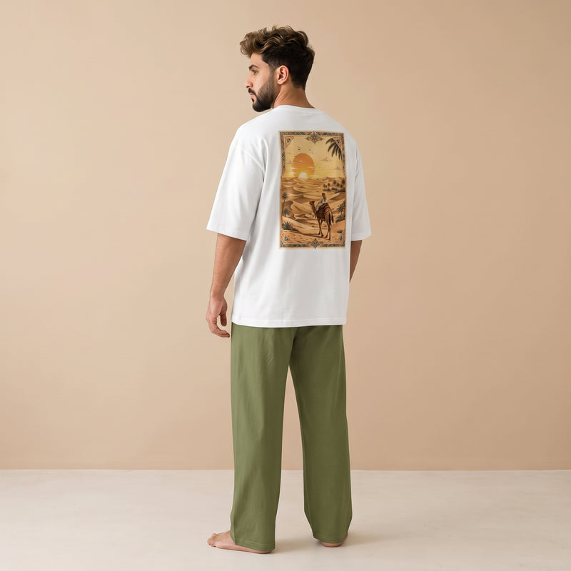 Man wearing a white oversized T-shirt with a desert sunset and camel rider graphic on the back, paired with olive green wide-leg pants.