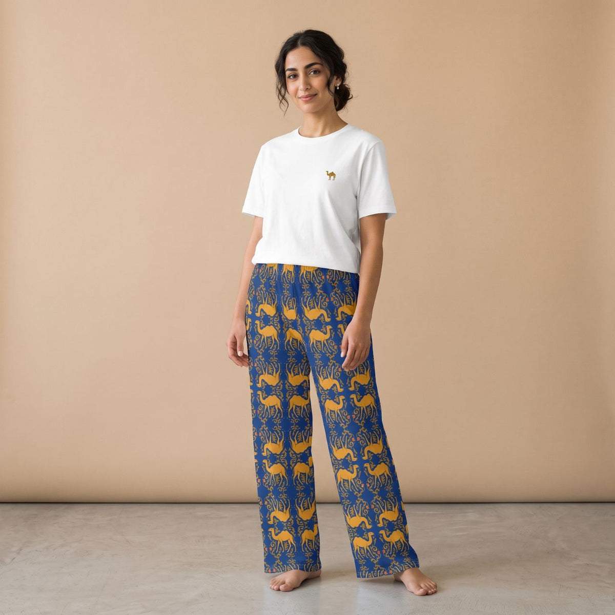Model wearing a white camel motif T-shirt and blue pants with golden camels and arabesque patterns, front view.