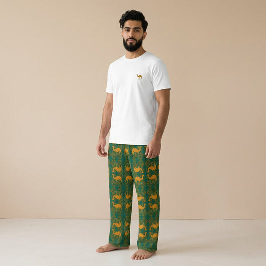 Man wearing a white T-shirt with a small gold camel motif and green trousers patterned with gold camels against a beige background.