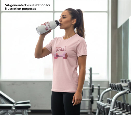 Woman in a gym wearing a pink t-shirt with a dumbbell graphic, drinking from a white water bottle.