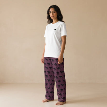 A woman stands barefoot in a studio wearing a white short-sleeve T-shirt with a small black camel print on the chest and purple pajama pants covered in a black camel print.