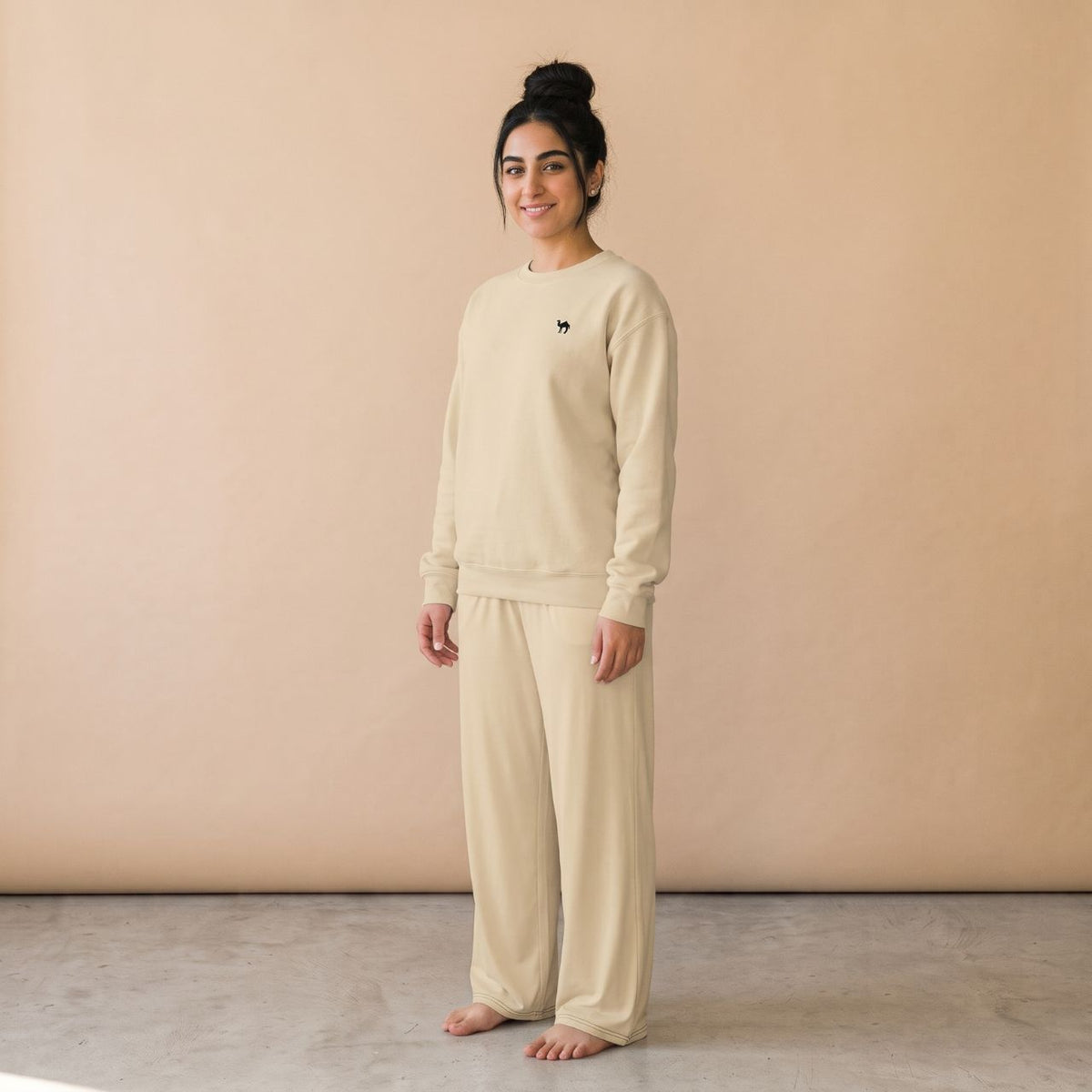 Model wearing a sand-coloured sweatshirt with a small black camel motif and matching plain wide-leg pants, front view.
