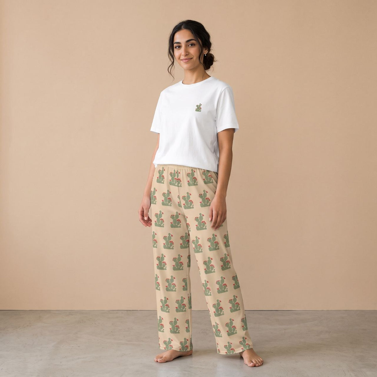 Model wearing a white T-shirt with a small cactus motif and cream pants with green flowering cactus prints, front view.