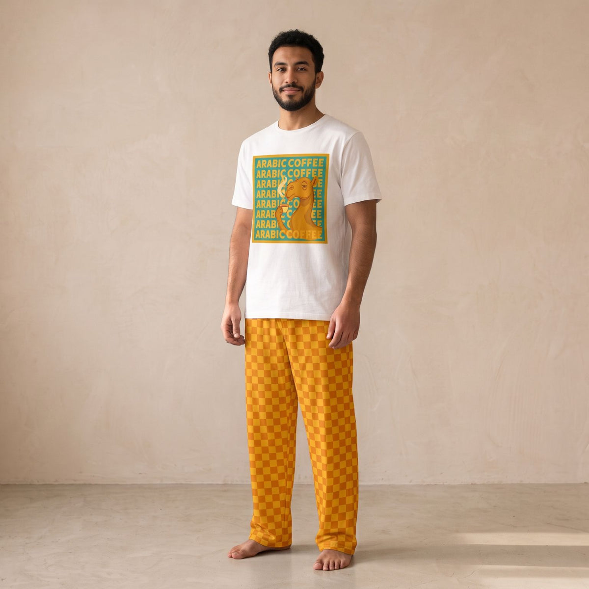 Man wearing a white camel and Arabic coffee graphic T-shirt with mustard-yellow checkerboard wide-leg pants.
