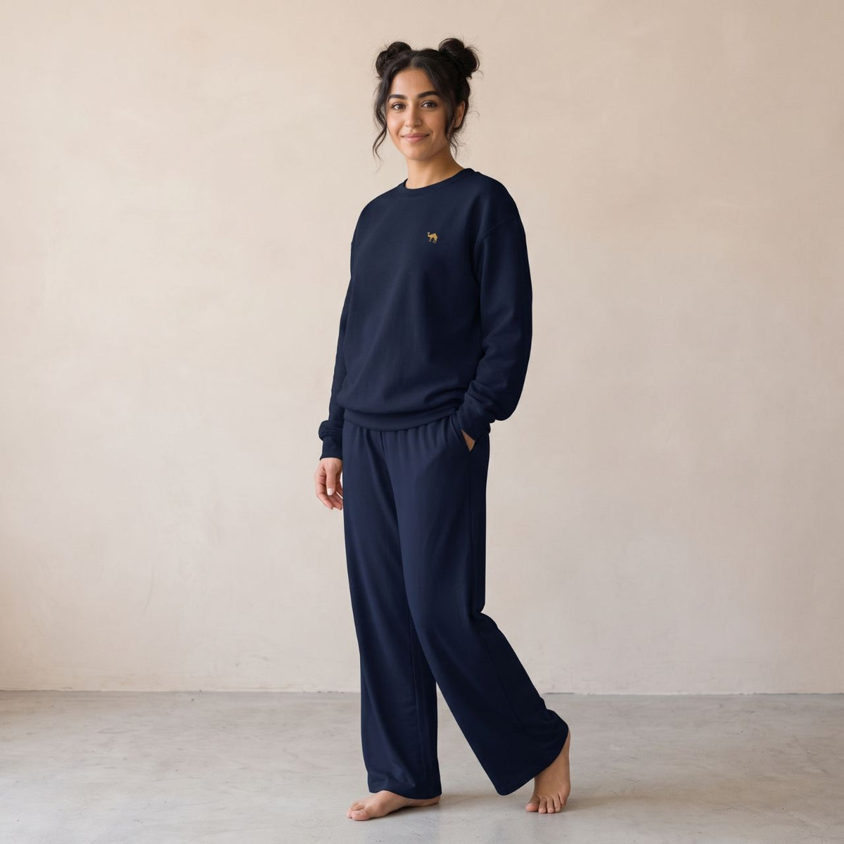 Model wearing a navy sweatshirt with a small gold camel chest motif and matching wide-leg pants.