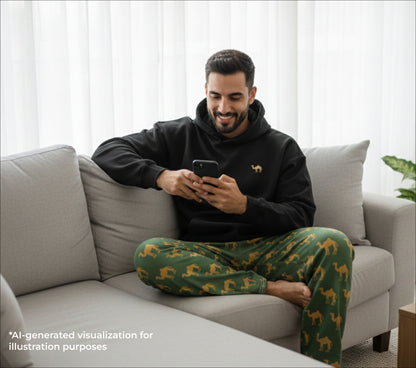 Man sitting on a couch wearing a black hoodie and green patterned pants, using a smartphone.