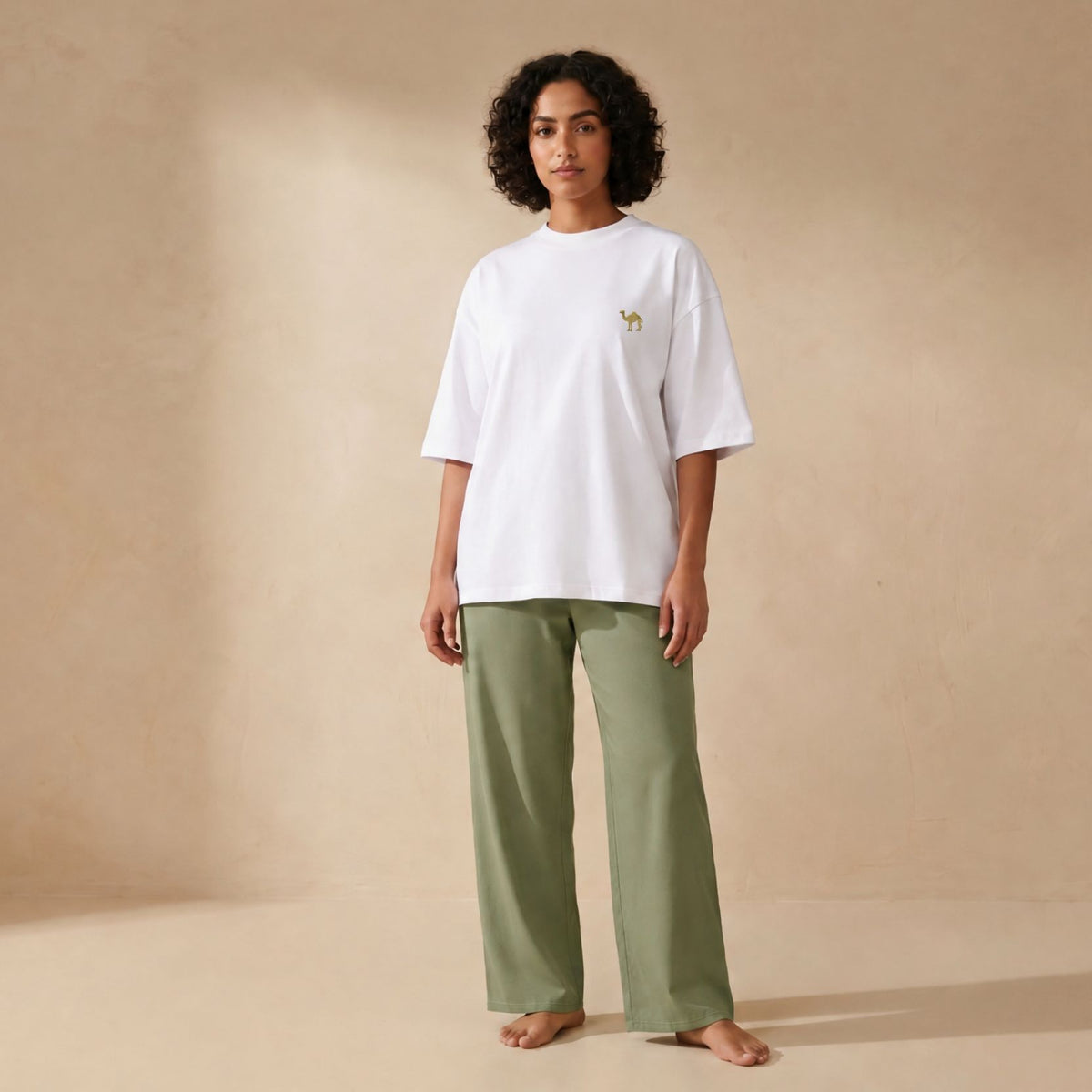 Model wearing a white oversized T-shirt with small camel embroidery and military green wide-leg pants, shown from the front.