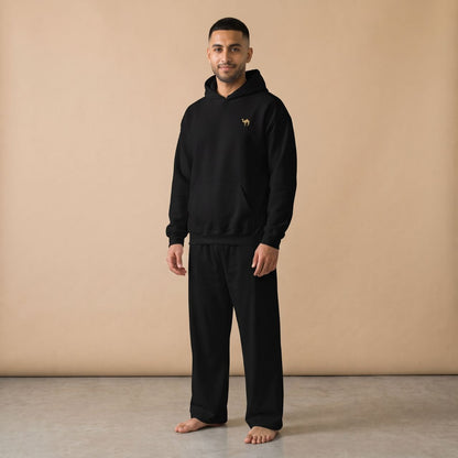 Model wearing a black hoodie with a small golden camel motif and plain black pants, front view.