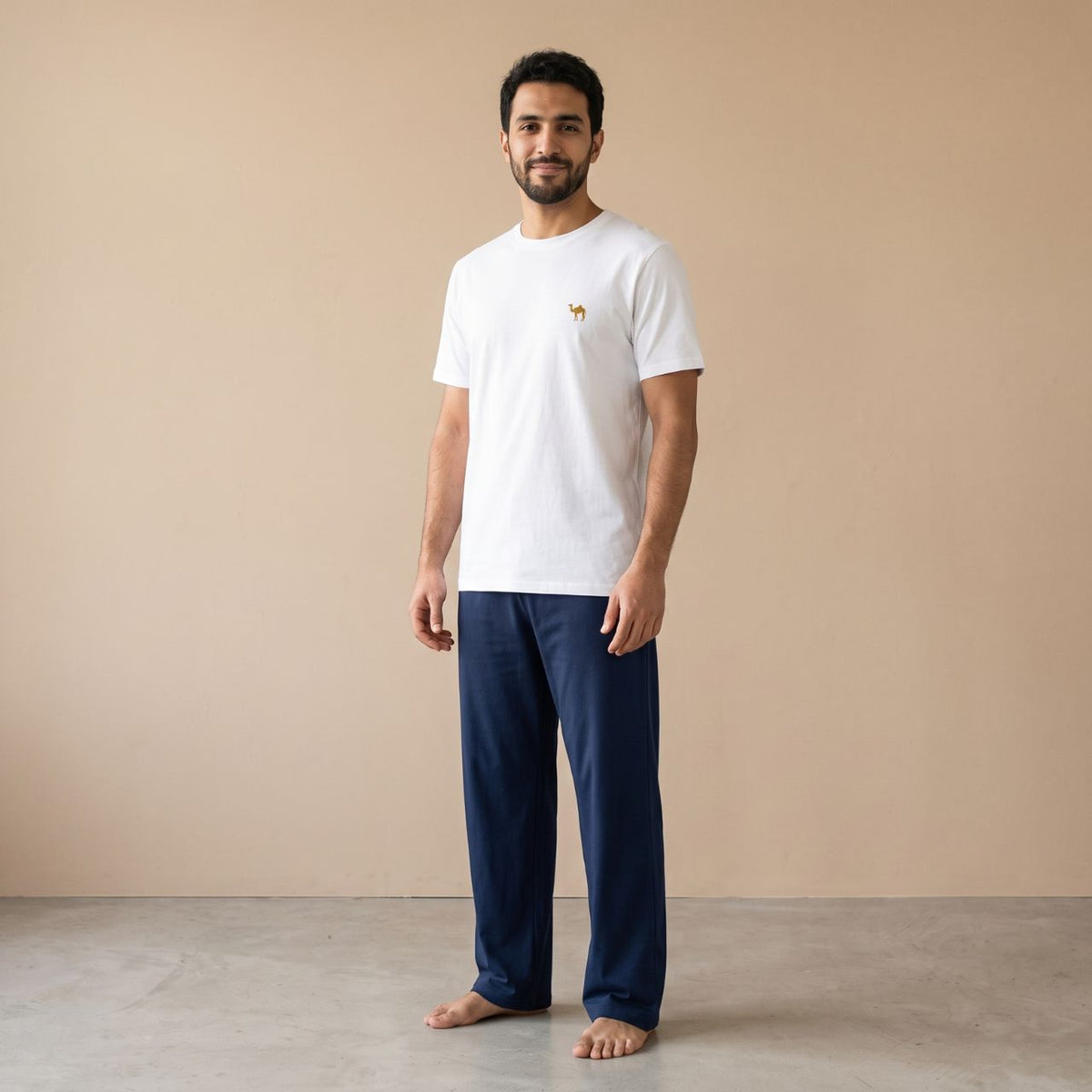 Model wearing a white T-shirt with a small camel motif and plain navy blue pants, front view.