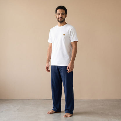 Model wearing a white T-shirt with a small camel motif and plain navy blue pants, front view.