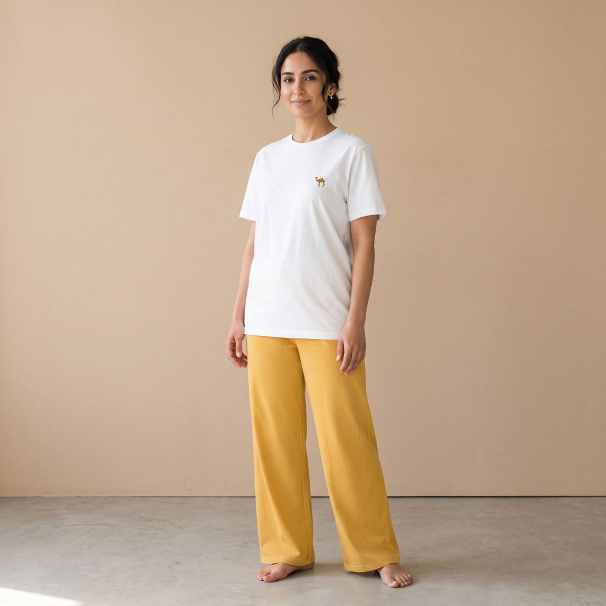 Model wearing a white T-shirt with a small camel motif and plain golden yellow wide-leg pants, front view.