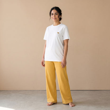Model wearing a white T-shirt with a small camel motif and plain golden yellow wide-leg pants, front view.