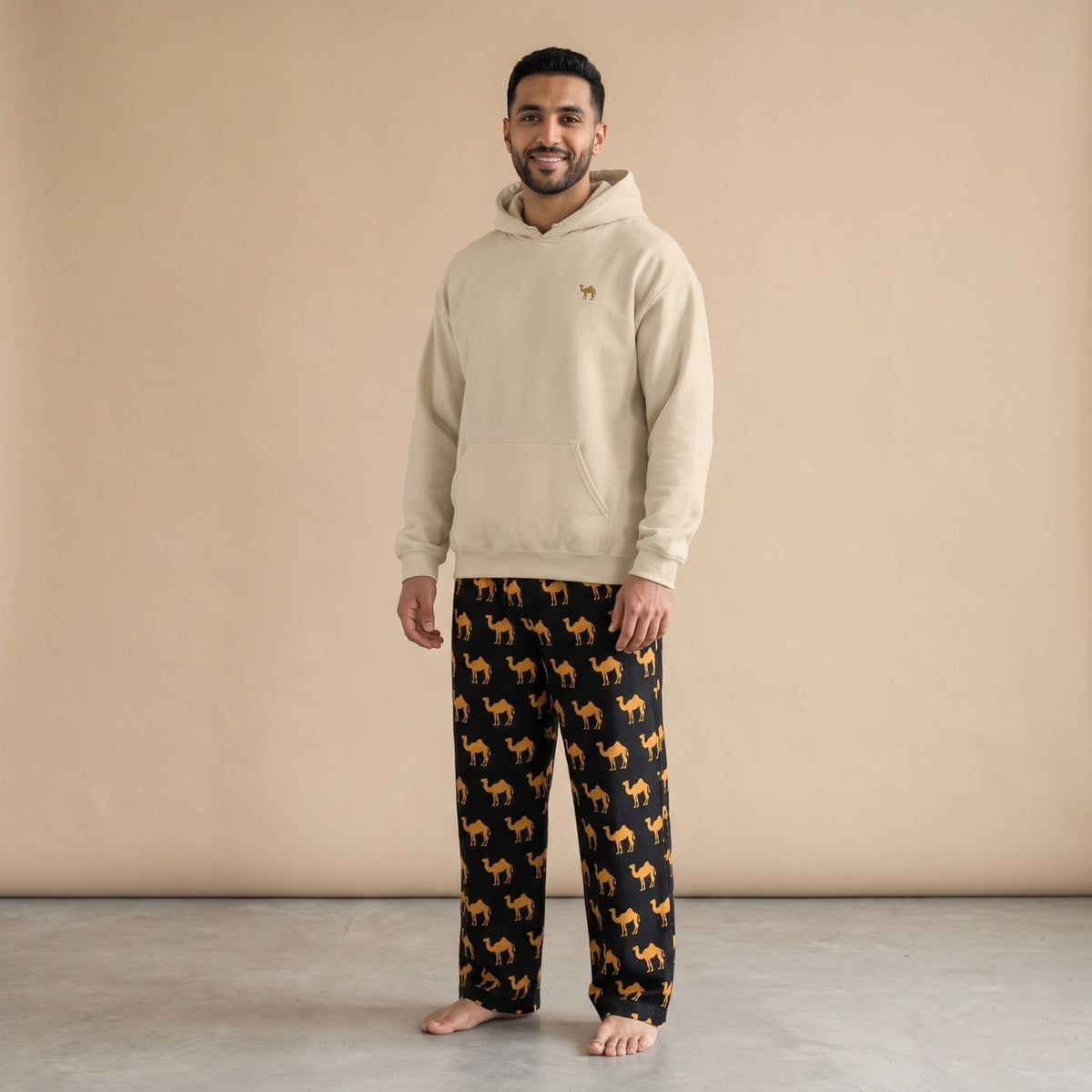 Model wearing a sand-coloured hoodie with a small camel motif and black pants with golden camel prints, front view.