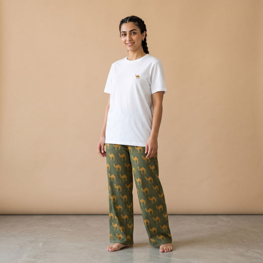 Model seated on a sofa wearing a white T-shirt and dark green pants with golden camel prints, using a phone.