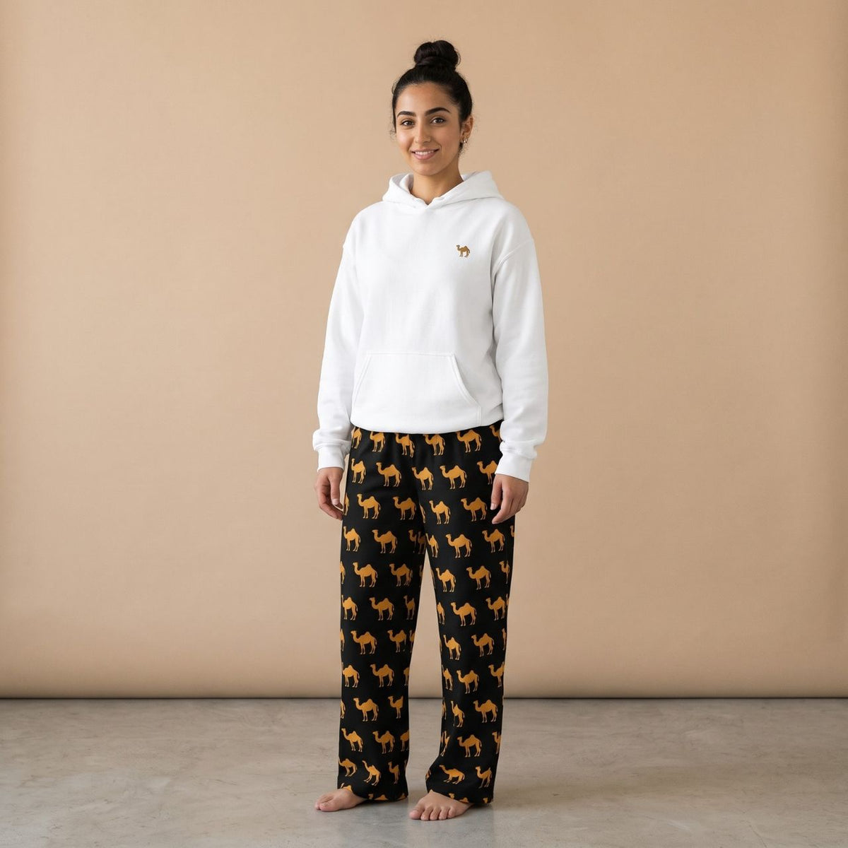 Model wearing a white hoodie with a small camel motif and black pants with golden camel prints, front view.