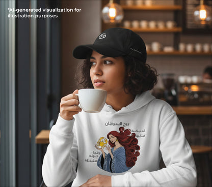 Woman in a cafe wearing a hoodie with a a Cancer graphic design, holding a cup.