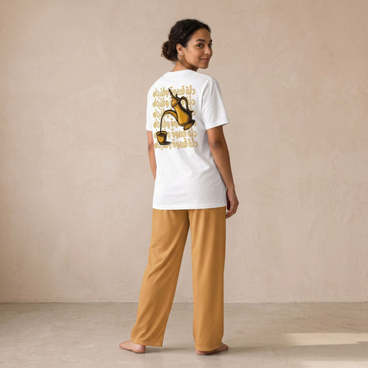 Woman, back view, wearing a white dallah and finjan graphic T-shirt with Arabic lettering (Dallat Gahwa & Finjan) and mustard-yellow wide-leg pants.
