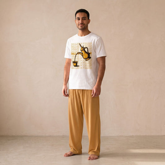 Man wearing a white T-shirt with a gold dallah and finjan graphic, paired with mustard-yellow wide-leg pants.