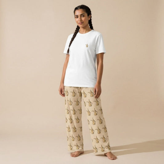 Model wearing the Dallat Gahwa set: a white T-shirt with a small gold coffee pot motif and beige wide-leg pants with an all-over Arabic coffee pot print.