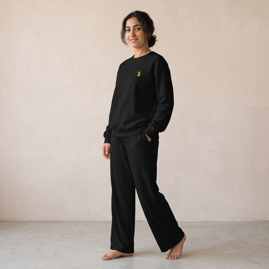 Model wearing a black sweatshirt with a small gold dallah coffee pot chest motif and matching wide-leg pants.