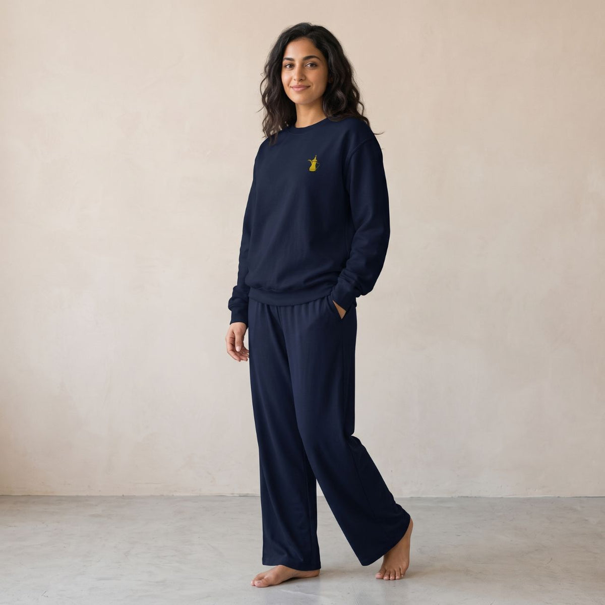 Model wearing a navy sweatshirt with a small gold dallah coffee pot chest motif and matching wide-leg pants.