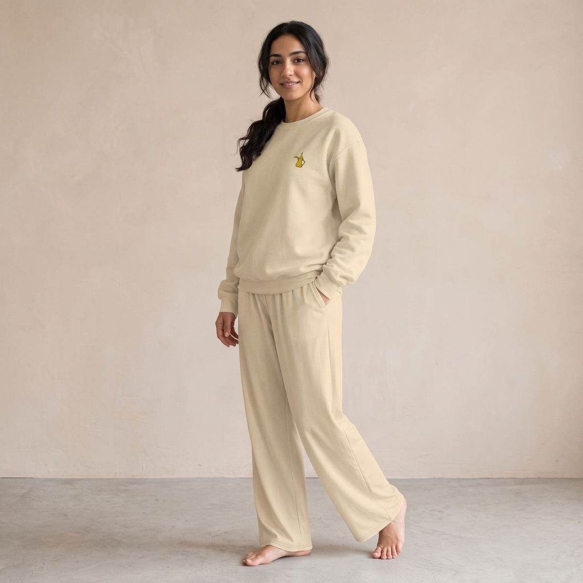 Model wearing a sand-coloured sweatshirt with a small gold dallah coffee pot chest motif and matching wide-leg pants.