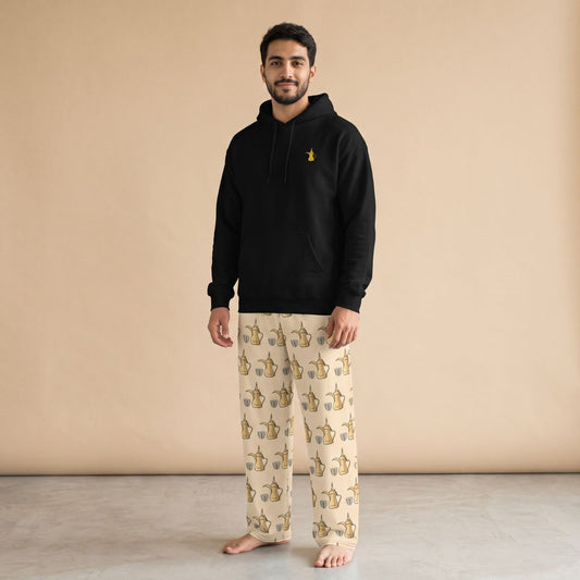 Model wearing a black hoodie with a golden dallah motif and cream pants with a dallah pot and finjan cup prints, front view.