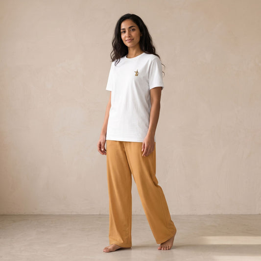Woman wearing a white T-shirt with a small dallah coffee pot motif and plain light-brown wide-leg pants.