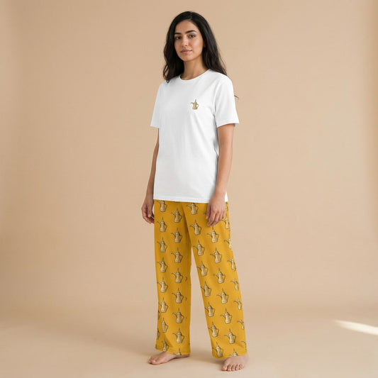 Model wearing a white T-shirt with a small Arabic coffee pot motif and mustard-yellow wide-leg pants with a matching all-over pattern.
