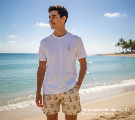 Man standing on a beach wearing a white t-shirt and dallat gahwa patterned shorts with a clear blue sky and ocean in the background.