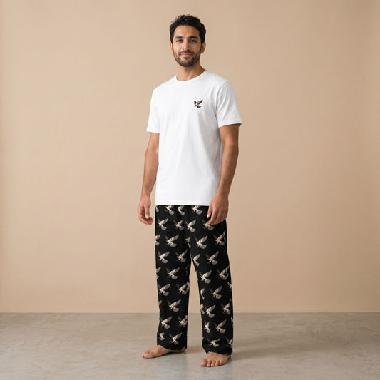 Model wearing a white T-shirt with a small falcon motif and black pants with an all-over flying falcon print, front view.