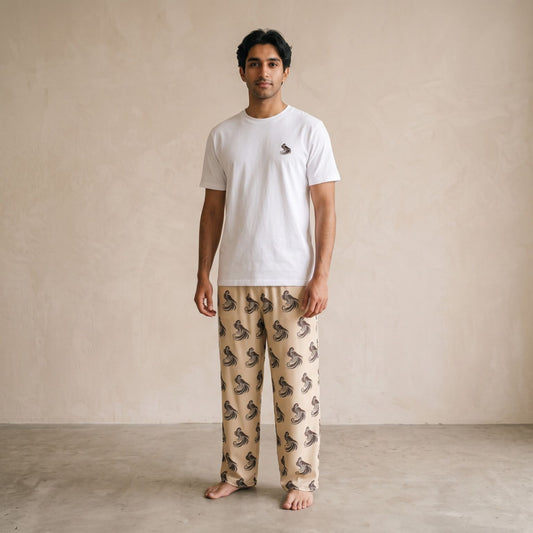 Model wearing a white T-shirt with a small falcon motif and beige pants with an all-over falcon print, front view.