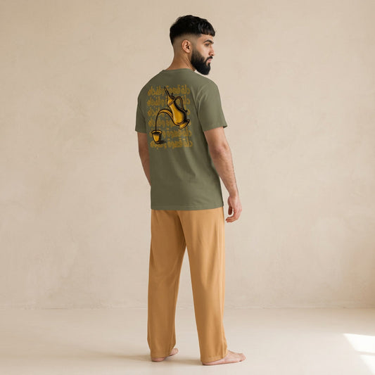 Model wearing a khaki T-shirt with a gold dallah and finjan graphic and Arabic lettering on the back, paired with light brown pants.