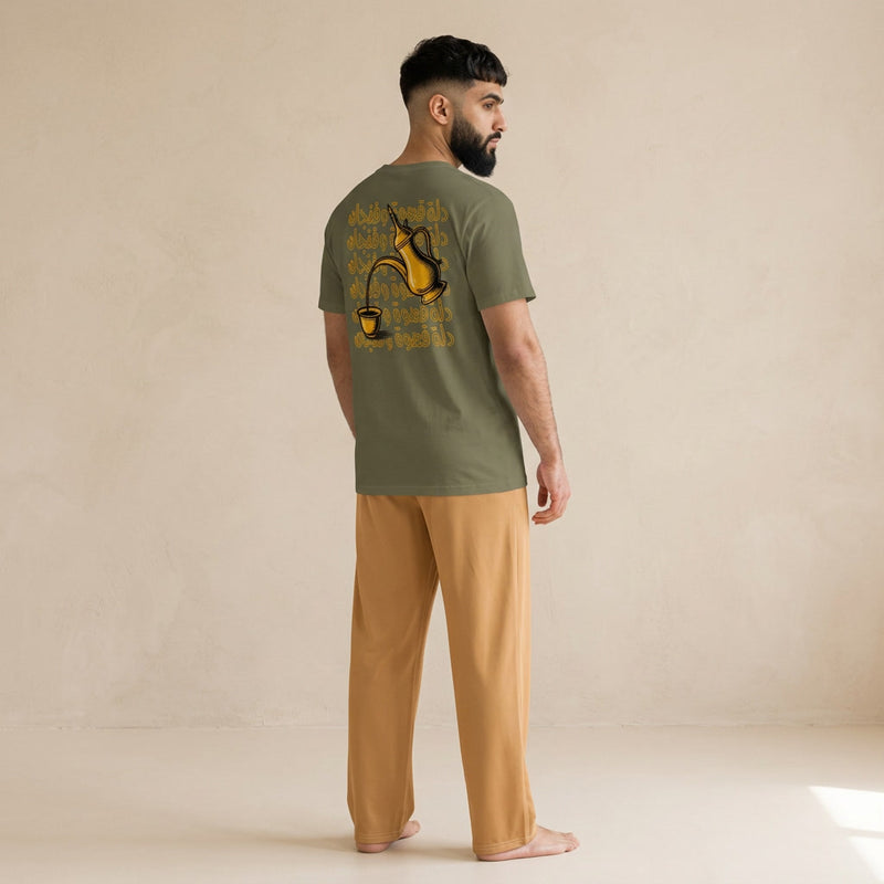 Model wearing a khaki T-shirt with a gold dallah and finjan graphic and Arabic lettering on the back, paired with light brown pants.