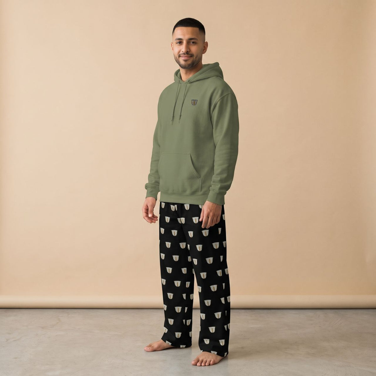 Model wearing an khaki green hoodie with a small finjan cup motif and black pants with white finjan cup prints, front view.