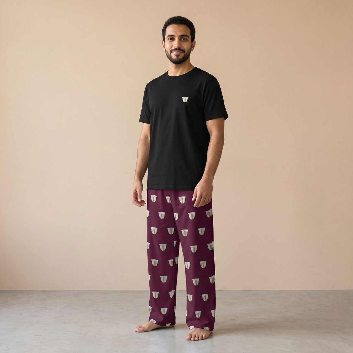 Model wearing a black T-shirt with a small finjan cup motif and maroon pants with white finjan cup prints, front view.