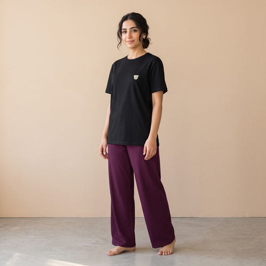 Model wearing a black T-shirt with a small finjan cup motif and plain maroon wide-leg pants, front view.
