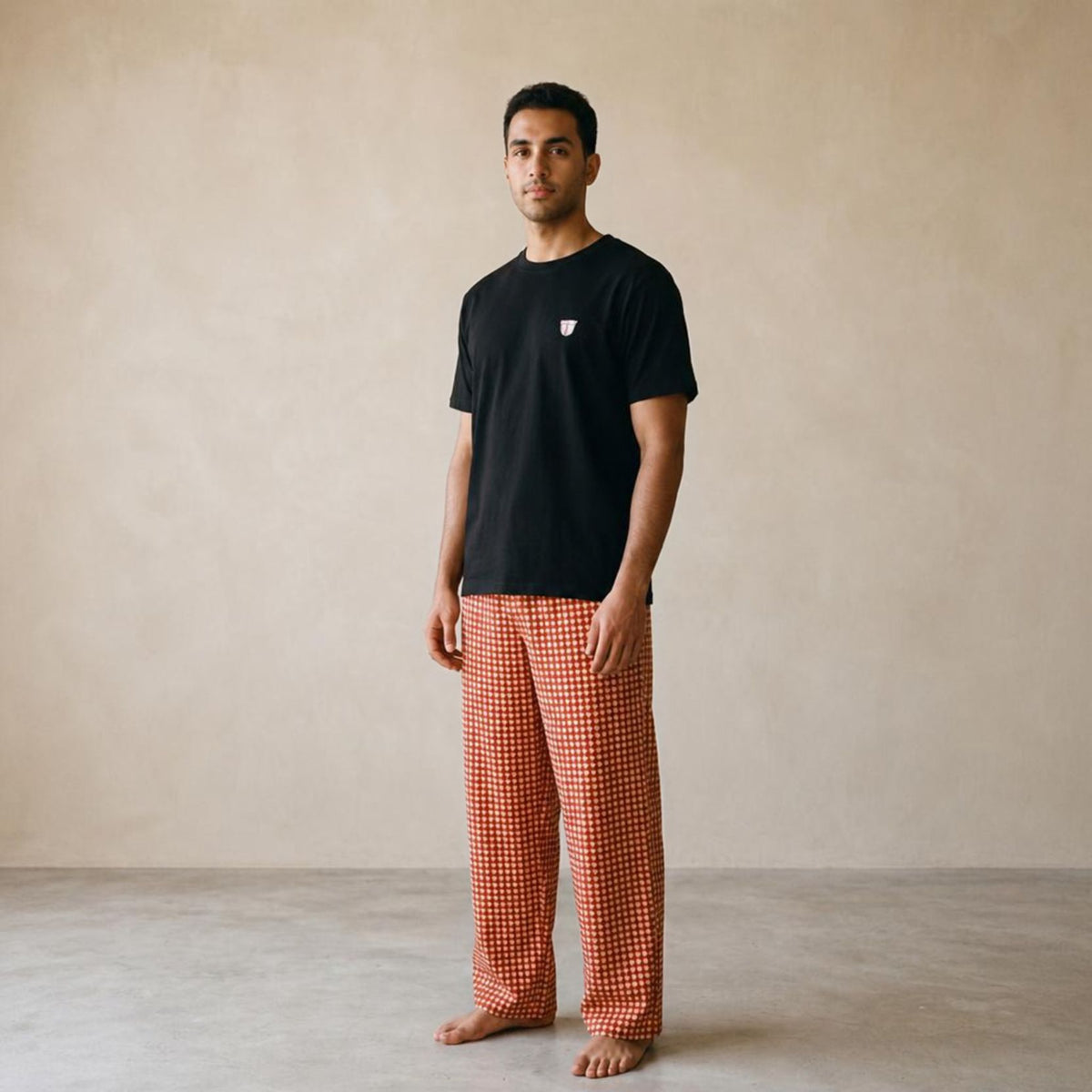 Model wearing a black Finjan T-shirt with a small chest motif and red and beige triangle-checkered wide-leg pants.