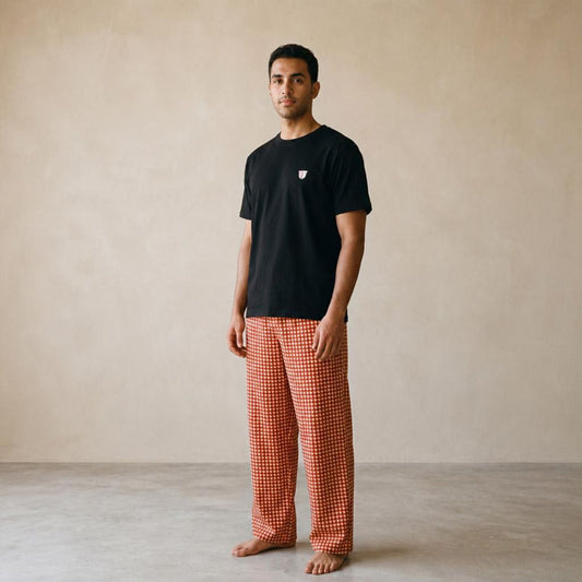 Model wearing a black Finjan T-shirt with a small chest motif and red and beige triangle-checkered wide-leg pants.