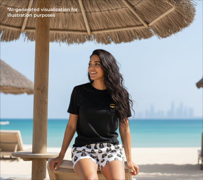 Woman in black shirt and golden burqa-patterned shorts standing under a thatched umbrella on a beach with ocean view.