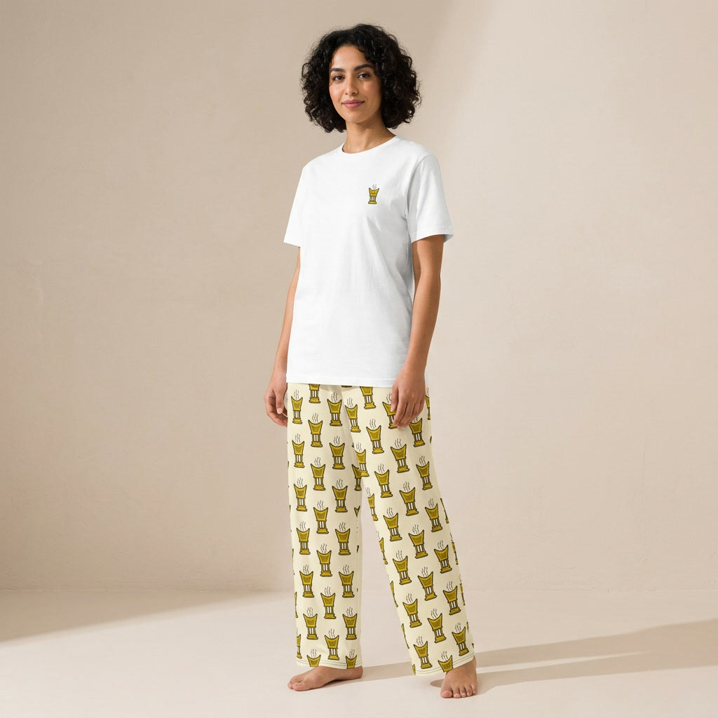 Model wearing a white T-shirt with a small yellow mubkhar motif and cream wide-leg pants with a repeating yellow mubkhar pattern.