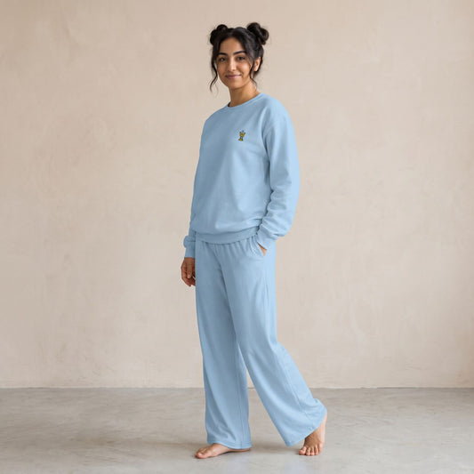 Model wearing a light blue sweatshirt with a small gold Mubkhar chest motif and matching wide-leg pants.
