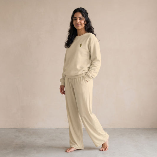 Model wearing a sand-coloured sweatshirt with a small gold Mubkhar chest motif and matching wide-leg pants.